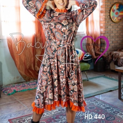 Mulher a usar vestido comprido com padrão de arabescos castanho e detalhes laranja, em ambiente interior rústico