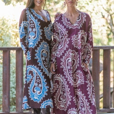 Duas mulheres com vestidos compridos de padrão paisley castanho-azul e vinho-bege com botas pretas.