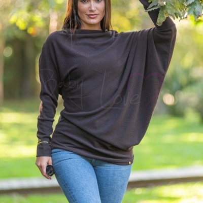 Mulher com camisola castanha e jeans azul a segurar ramo ao ar livre.