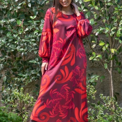 Vestido comprido vermelho com padrão alaranjado e mangas compridas, usado com botas castanhas em ambiente de jardim.