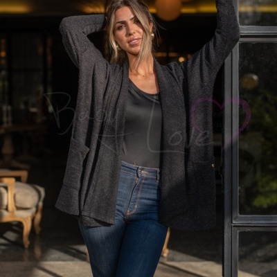 Mulher com casaco cinzento escuro de malha, t-shirt preta e jeans azuis em ambiente interior