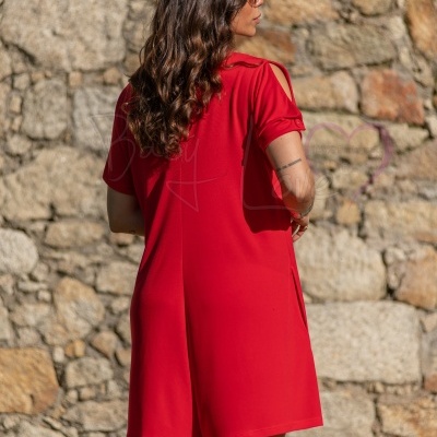 Vestido curto vermelho com abertura nos ombros e abotoamento na manga, mulher de costas em fundo de parede de pedra.