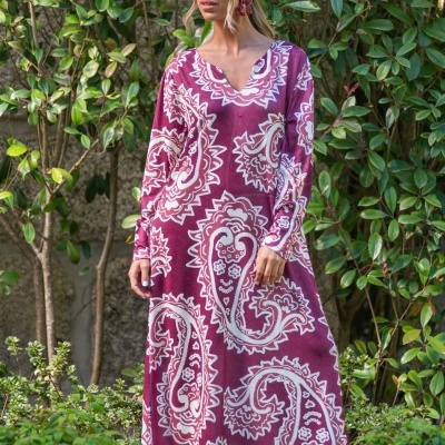 Vestido longo vinho com padrão branco paisley usado por mulher junto a plantas verdes