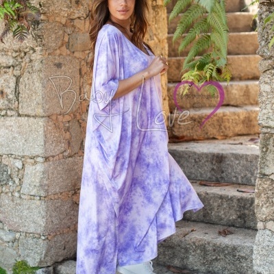 Mulher com vestido largo lilás tie-dye e ténis brancos em escadaria de pedra