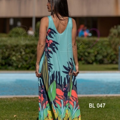 Vestido comprido azul com estampa tropical colorida, modelo vista de costas no relvado junto à piscina.