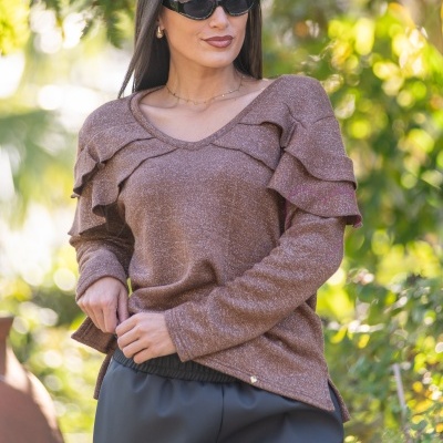 Mulher com camisola castanha com folhos e calças pretas em ambiente exterior