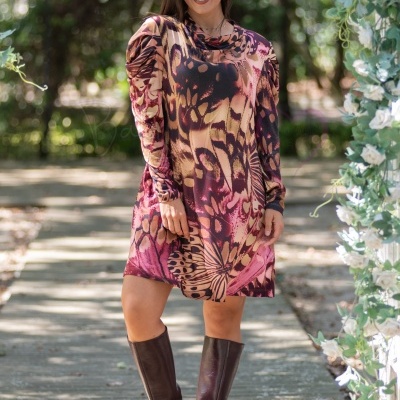 Mulher com vestido curto estampado de manga comprida e botas castanhas em ambiente natural com flores brancas ao lado