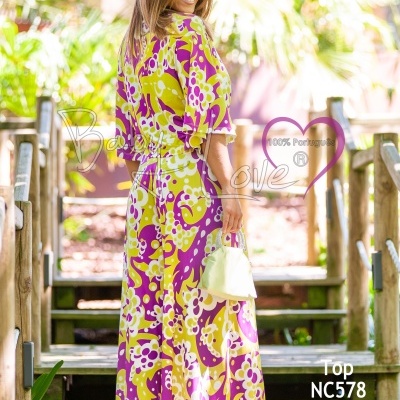 Vestido longo colorido amarelo, roxo e branco com padrão floral, modelo feminino em ambiente exterior com escadas de madeira.