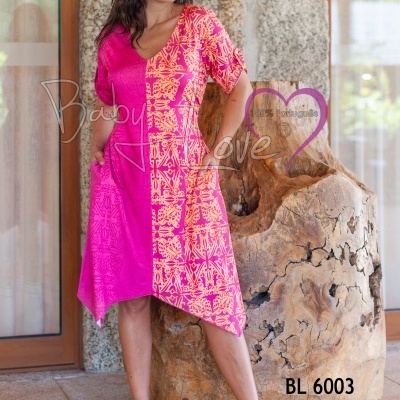 Vestido midi rosa e laranja com padrão geométrico, modelo em ambiente com parede de pedra e janela de vidro.