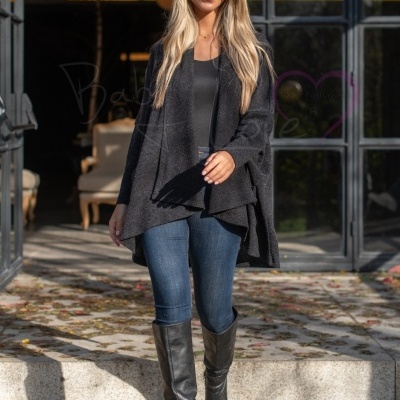 Mulher usando cardigan preto assimétrico, jeans azul e botas pretas em ambiente exterior