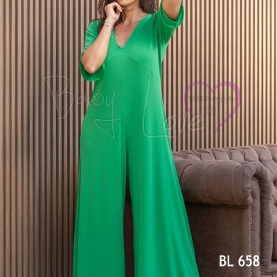 Macacão verde com mangas curtas e decote em V, parede de ripas castanha e sofá castanho