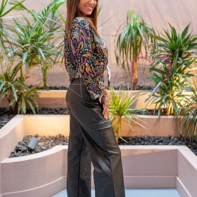 Mulher com túnica estampada e calça preta numa área com plantas e paredes cor de salmão