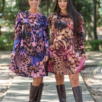 Duas mulheres com vestidos curtos com padrão de asas de borboleta e botas castanhas em passadiço de madeira