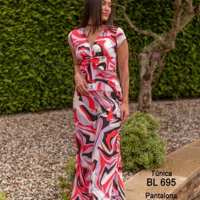 Mulher com túnica e pantalona com padrão abstrato vermelho, rosa, branco e preto num jardim