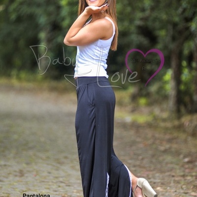 Mulher a usar pantalona preta com detalhe lateral de lantejoulas, top branco e sapatos de salto altos bege, em ambiente exterior com vegetação.