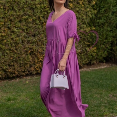 Mulher a usar vestido rosa roxo comprido, com mala branca e sandálias roxas, no jardim
