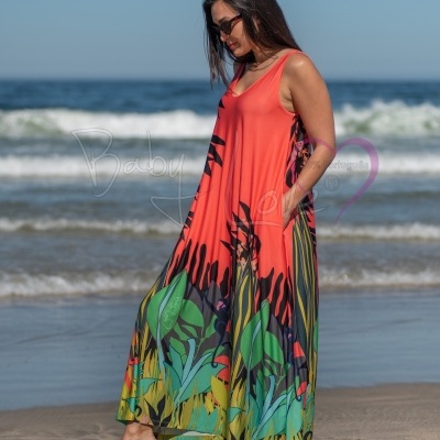 Mulher na praia a usar vestido comprido de alças com padrão tropical multicolorido.