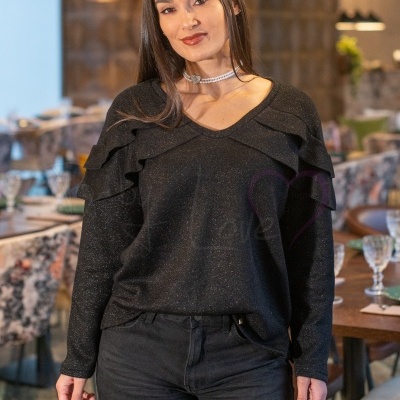 Mulher com sweatshirt preta brilhante com folhos e calças pretas num restaurante