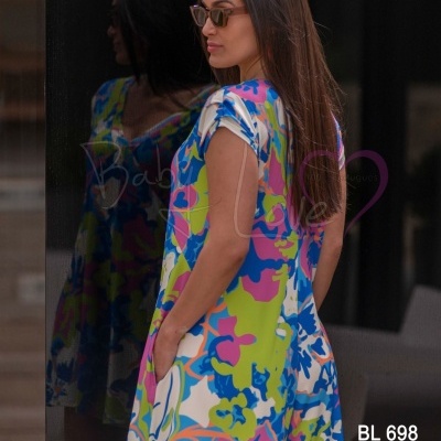 Vestido curto floral colorido com bolsos e gola em V em mulher com óculos de sol junto a parede espelhada
