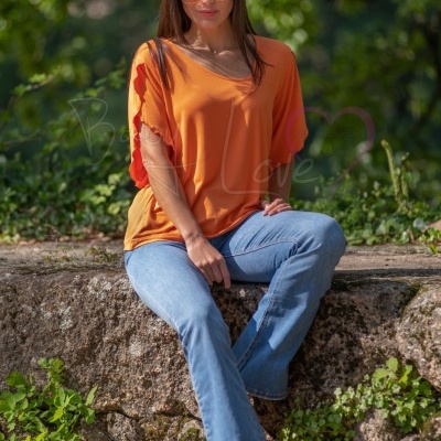 Mulher com túnica laranja e calças de ganga sentada numa pedra em ambiente natural