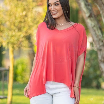 Mulher com t-shirt coral de decote em V e calças brancas ao ar livre
