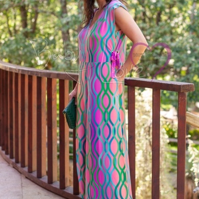 Mulher de vestido comprido colorido com padrão geométrico, sapatos e clutch verdes, em varanda exterior