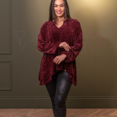 Mulher com túnica bordô de veludo e calças pretas em ambiente interior