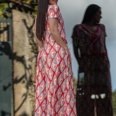 Vestido comprido colorido com padrão geométrico em mulher junto a vidro