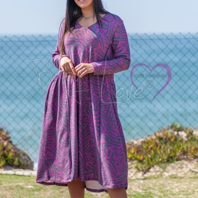 Vestido roxo e rosa com padrão geométrico, chapéu preto e botas junto ao mar