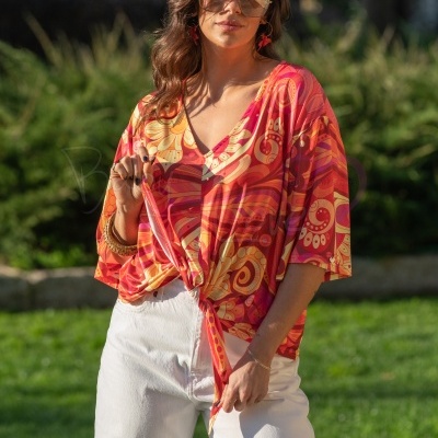 Mulher com blusa colorida com padrão psicadélico e calças brancas ao ar livre