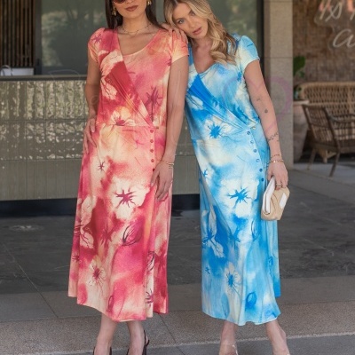 Duas mulheres com vestidos florais rosa e azul e salto alto num ambiente interior.