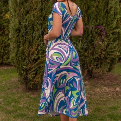 Vestido midi com padrão abstrato azul, verde, lilás e branco e sandálias lilás, em jardim com árvores verdes.