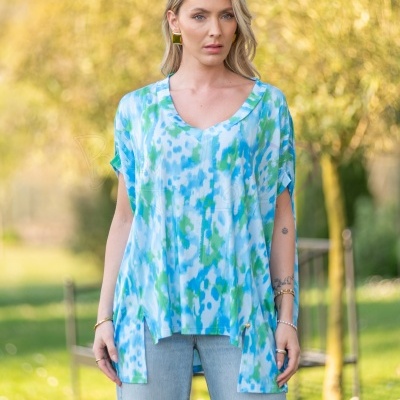 Mulher com blusa leve azul, verde e branca com decote em V e jeans claros em ambiente exterior