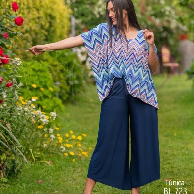 Mulher a usar túnica azul com padrão zigzag e calças culotte azul escuro num jardim florido.