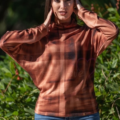 Mulher com túnica castanha xadrez e jeans em ambiente exterior verde