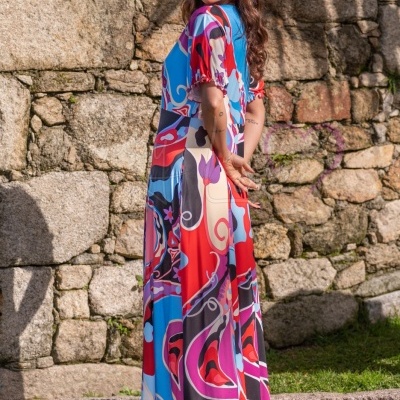 Vestido comprido colorido usado por mulher ao ar livre junto a parede de pedra.