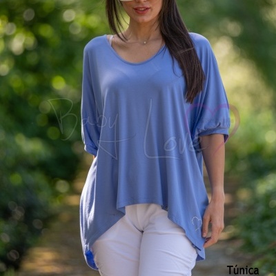 Mulher com túnica azul e calça branca em ambiente natural, usando óculos de sol grandes