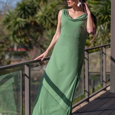 Mulher com vestido verde claro e óculos castanhos encostada em varandim exterior com árvores ao fundo