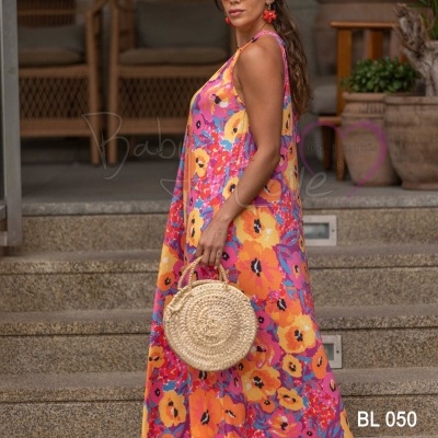 Mulher com vestido floral colorido, bolsa redonda de palha e óculos de sol numa escadaria