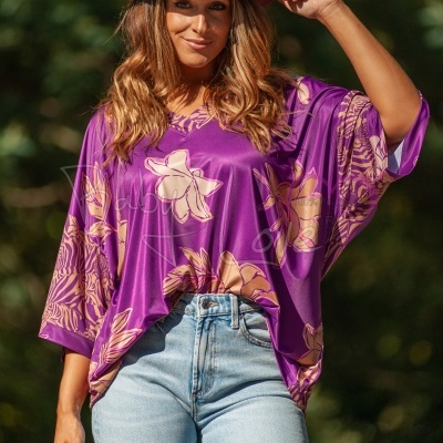 Blusa roxa com flores bege usada por mulher com chapéu vinho e calças de ganga claras