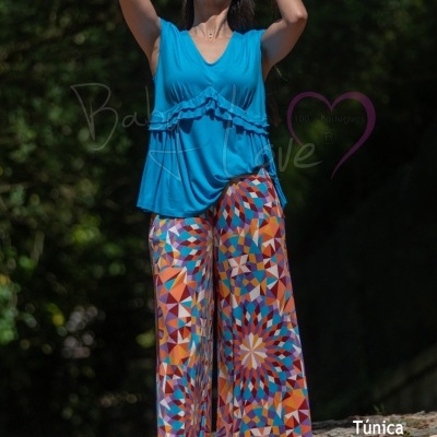Mulher com túnica azul e calças largas com padrão geométrico colorido em ambiente exterior