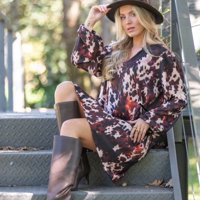 Mulher com vestido padrão animal e botas castanhas sentada numa escada metálica