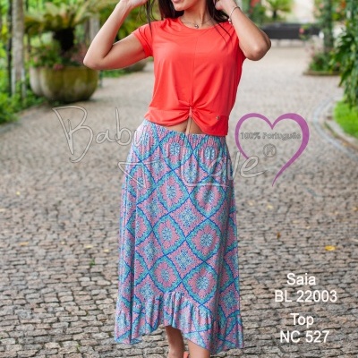 Mulher com saia azul e rosa e top laranja em passeio com vegetação