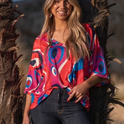 Mulher a usar t-shirt colorida com padrão abstrato e calças de ganga junto a uma palmeira