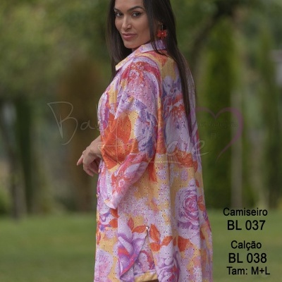 Camisa floral colorida com botões e furos decorativos, usada por modelo em ambiente verde