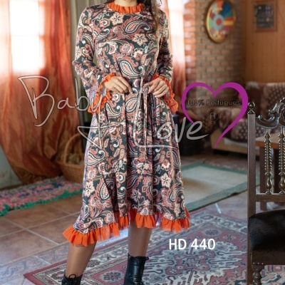 mulher com vestido paisley castanho e laranja em sala com tapetes e sofás