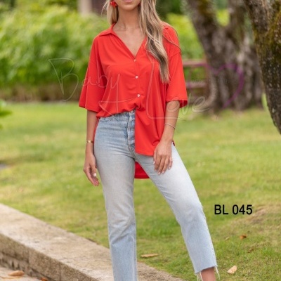 Mulher vestindo blusa vermelha e jeans azul claro em ambiente exterior com árvores