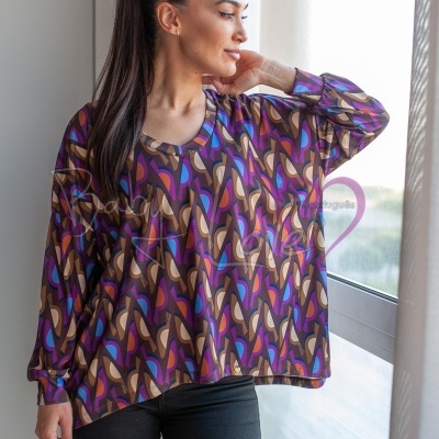 Blusa feminina com padrão geométrico colorido e calças pretas numa pessoa junto a uma janela