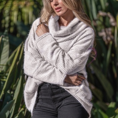 Mulher com camisola de malha branca e calças pretas ao ar livre com vegetação ao fundo
