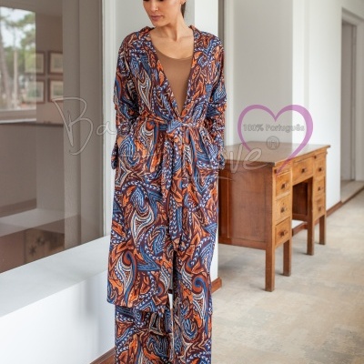 Mulher com kimono, body e calças coloridos em padrão abstrato num interior com mobília de madeira